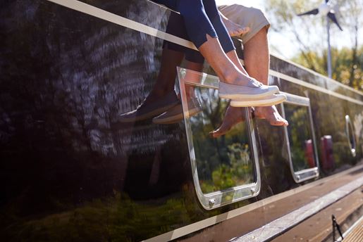 The legs of two people sat on top of a canal boat in the sun.